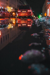 Red car drives along a narrow street at night in winter with thawed snow, photo from the lower angle