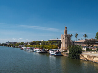 Fototapeta na wymiar Torre del Oro (tower of gold) next to the Guadalquivir river with boats and blue sky