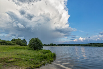 Summer landscape, rain clouds over the lake. Bright green on the shore of the reservoir, after the rain. Large thundercloud.