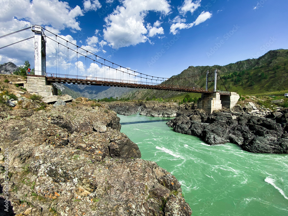 Wall mural Green river flowing through large rocks - mountains in the background