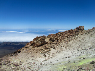 Fototapeta na wymiar The rocky peak of the Teide volcano with yellow sulfur emissions, a view of the land covered with clouds