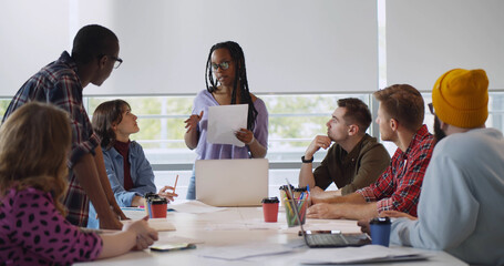 African female colleague presenting new start up project to coworkers in creative office