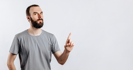 Portrait of cheerful young handsome man smiling looking at camera pointing finger upwards on white background with space for advertising mock up
