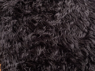 Black animal wool texture background. Close-up texture of plush fluffy fur rug for product backdrop, straight view