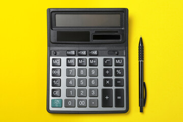 Calculator and pen on yellow background, flat lay