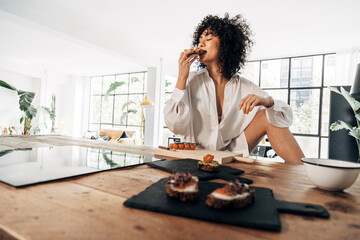 Fototapeta na wymiar Young mixed race woman biting avocado toast for breakfast in a bright loft apartment