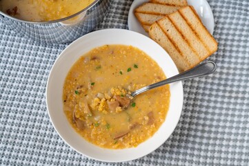 Soup from orange lentil, bread and pot on kitchen table.