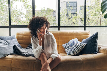Young african american woman sitting sofa talking with a friend on cellphone at home.