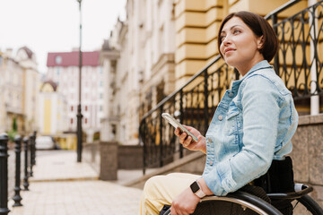 Brunette woman using mobile phone while sitting in wheelchair