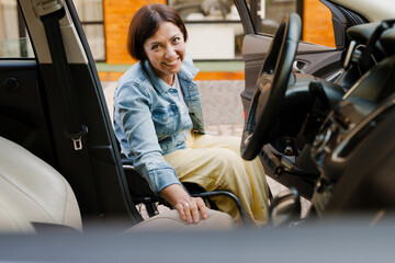 Brunette woman in wheelchair getting into car on city street
