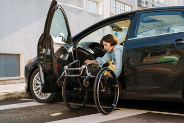 Fototapeta na wymiar Brunette woman holding wheelchair while getting into car on city street