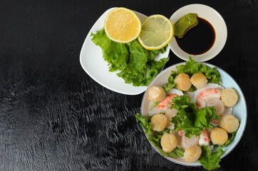 Fried scallop meat with boiled shrimps in a ceramic plate with lettuce, lemon, soy sauce and wasabi.