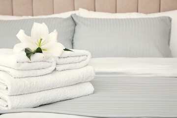 Fototapeta na wymiar Stack of fresh towels with flower on bed indoors, space for text