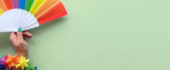 LGBTQ community pride banner. Hand with rainbow flag, flower garland and fake nails in colors of rainbow. Concept shot. Top view on mint blue background. Panoramic image, copy-space, place for text.