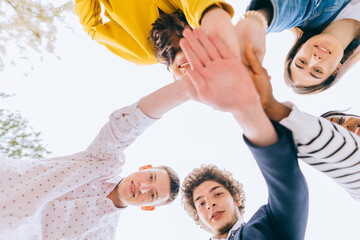 A group of five friends students man and women smiling and looking down at camera, handshake high five teamwork concept of tenagers friendship, sunny autumn mood. Bottom view.