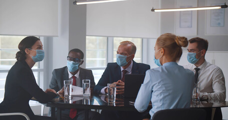 Group of multiethnic business people in meeting wearing safety mask in boardroom.