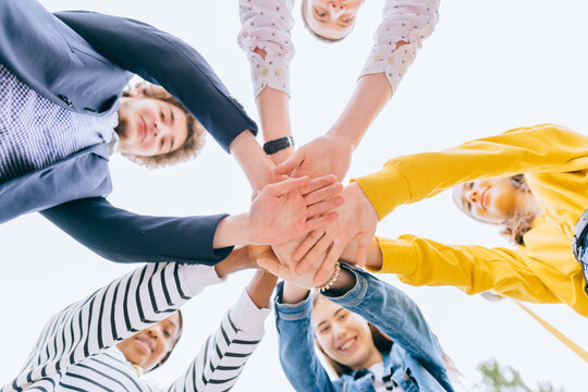 A group of five friends students man and women handshake high five teamwork concept of tenagers friendship, sunny autumn mood. Bottom view.