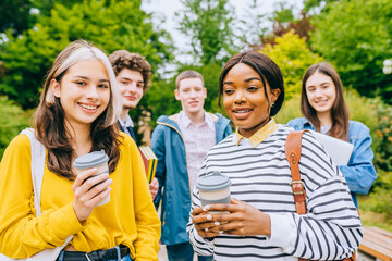 People, friendship, communication and international concept. Group of happy students friends walking along spring park and drinking coffee, looking at camera and smiling.