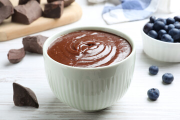 Delicious chocolate cream and blueberries on white wooden table, closeup