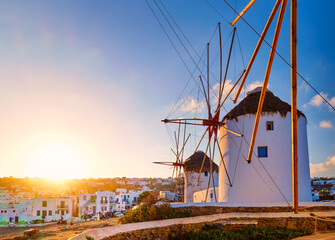 Famous tourist attraction of Mykonos, Greece. Traditional whitewashed windmills in row against sun. Summer, sunrise, travel destination, iconic view.