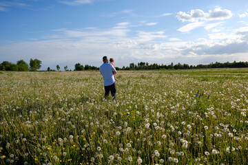 A father with short hair in a white T-shirt holds his little daughter in a pink dress in his arms...