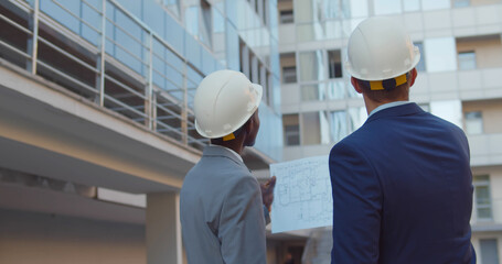 Back view of diverse industrial engineers planning on blueprint at work site.