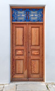 Old vintage wooden doors in light natural color decorated with blue forge-smithing metal ornament with monograms of capital letters M and X