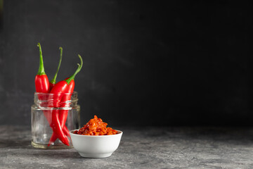 Harissa national hot sauce of Tunisia in a white plate with chilli peppers in a glass jar in a low key copy space for text