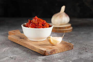 Harissa sauce, Ajvar or lutenitsa with a white plate on a wooden board with garlic in a low key