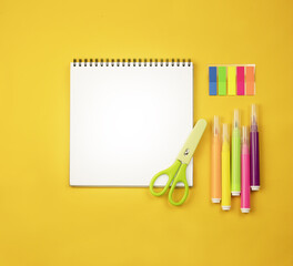 Back to school. Notepad on a yellow background, colored markers and green scissors. Colored stickers drawing set. School learning concept. Copy space.