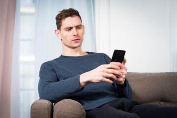 Portrait of sad unpleasant unhappy guy, young frowning man looking at screen of his cell mobile...