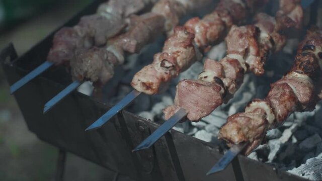 Shish kebab on sticks fried on coals in nature. Grilling tasty barbecue on black coals on mangal outdoor. Golden crust and smoke aroma. Barbecue on charcoal in the yard in nature with stew on skewers.