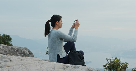 Woman sit on the rock and use cellphone to take photo on mountain