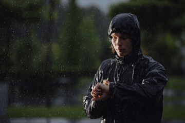 Man jogger looks a time on his watch under rain, flash light
