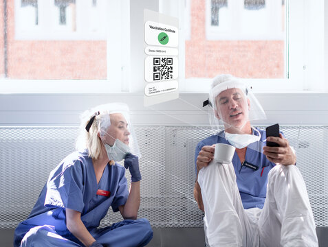 Doctors wearing personal protective equipment looking at cell phone with Covid-19 vaccine certificate