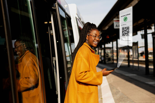 Smiling woman leaving bus at bus station with Covid-19 vaccine certificate on cell phone