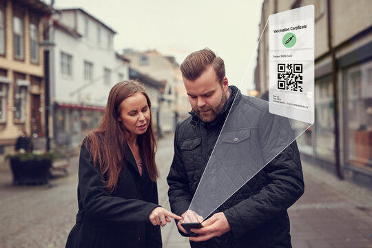 Man and woman standing in street and checking phone with Covid-19 vaccine certificate