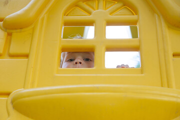 Kid plays in the yellow playground, looks out of the house