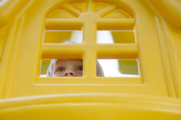 Little child plays in the yellow playground, looks out of the window