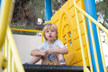 A caucasian child sits on a slide in the playground