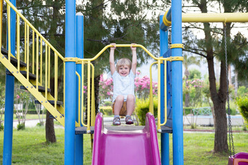 Happy child riding a slide in the playground against the background of purple flowers outdoors