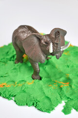 Toy elephant on green kinetic sand, children's games.