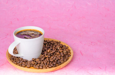 Coffee and coffee beans are placed on a round wooden tray. A bright pink background