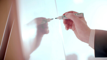 Close up of businessman hand holding marker and writing on whiteboard in office. 