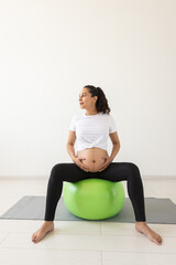 Fototapeta na wymiar A young pregnant woman doing relaxation exercise using a fitness ball while sitting on a mat.