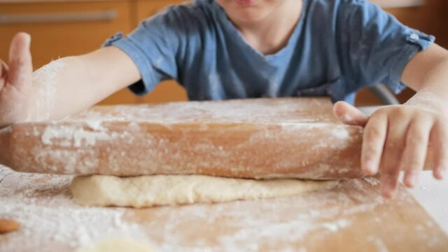 Closeup of little boy rolling dough with rolling pin for making pizza.