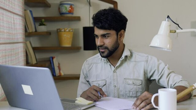 Indian male employee involved video call meeting on the laptop with work team,man using laptop for video connect,talking and taking notes,brainstorming online,Asian guy doing online study from home.