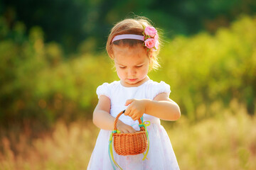 A small beautiful girl is holding a basket. The child is preparing for the celebration of Easter. Happy child on a walk.