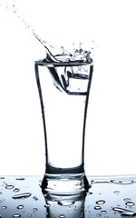 Ice in glass of water with splash on white background
