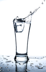Ice in glass of water with splash on white background